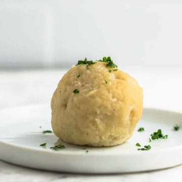 德国土豆饺子——Kartoffelklosse放在一个白盘子里。